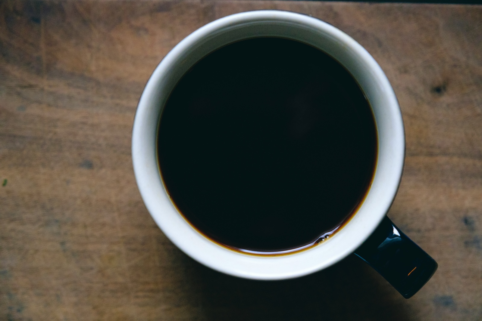 Overhead view of a cup of black coffee in a white ceramic mug on a wooden table.