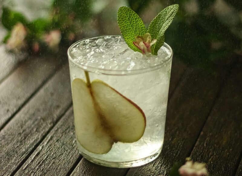 Refreshing cocktail with crushed ice, local pear, and garnished with fresh herbs, in a clear glass.
