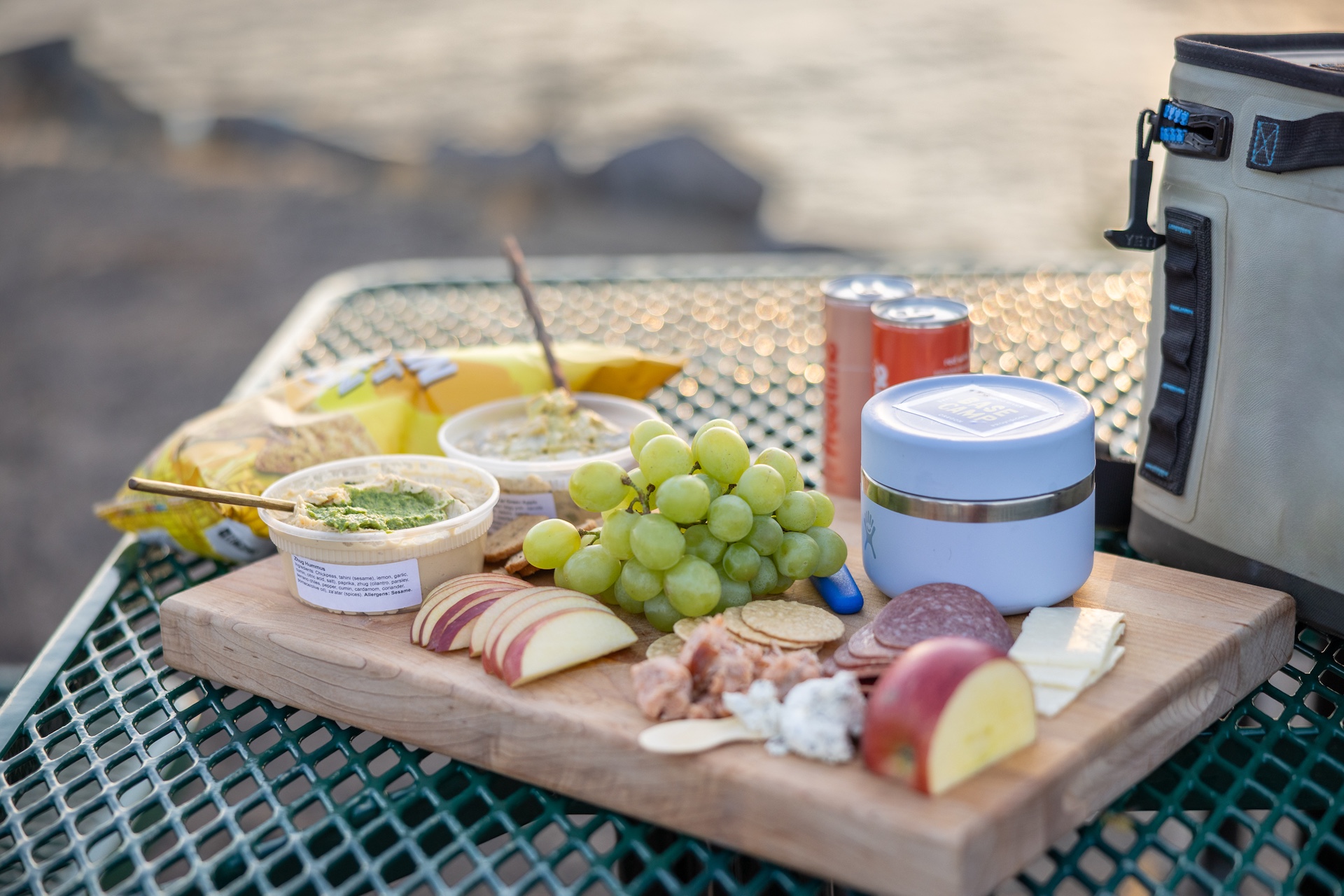 Charcuterie board with salami, cheese, grapes, apples and hummus on a picnic table with PNW vibes.