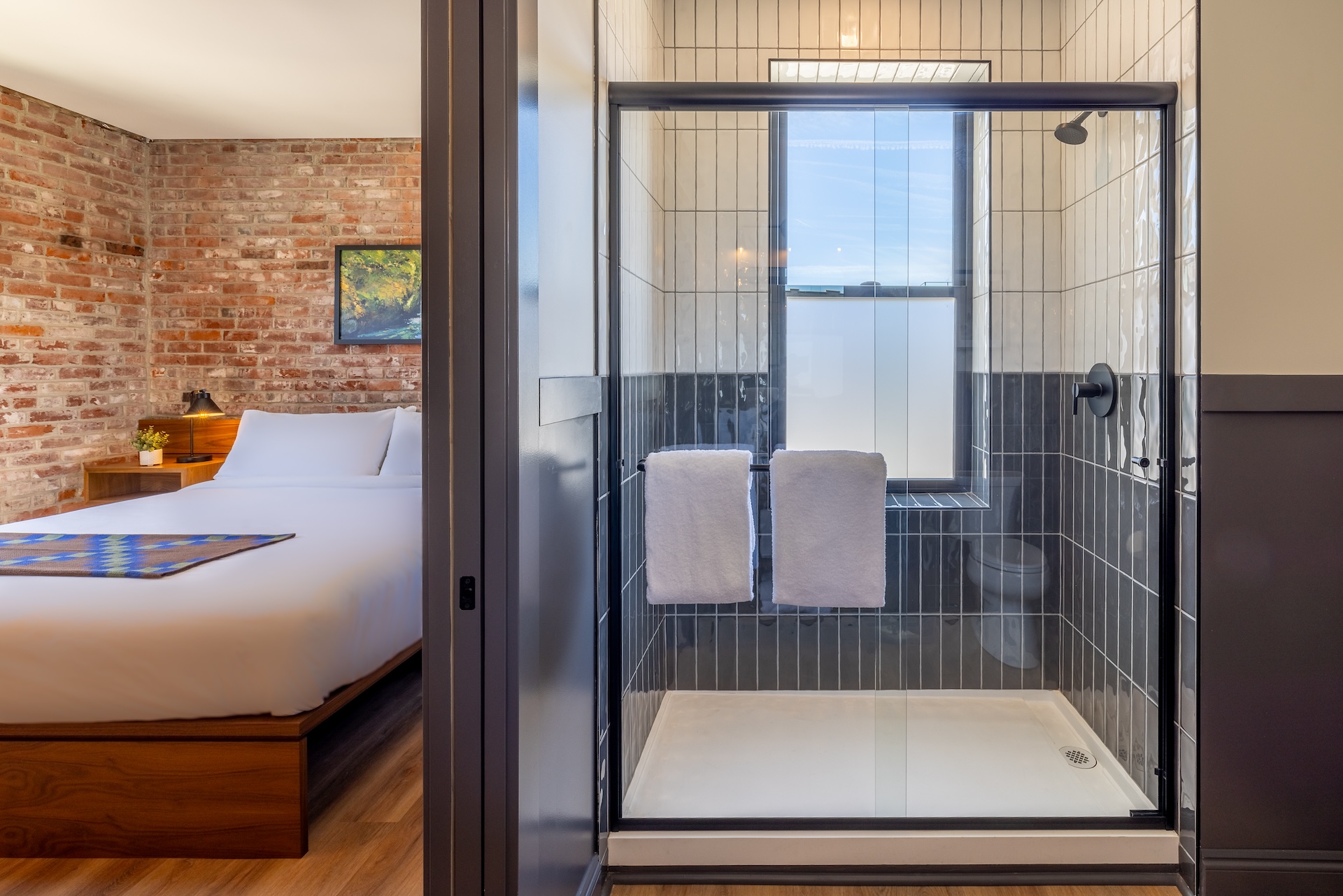 City View King guest room at Lightwell Hotel & Spa in Hood River featuring a modern tiled shower with glass doors and exposed brick bedroom wall.