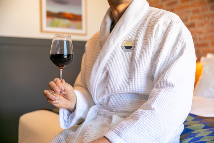 Guest in a Lightwell Hotel robe holding a glass of Oregon wine in a River View King guest room.
