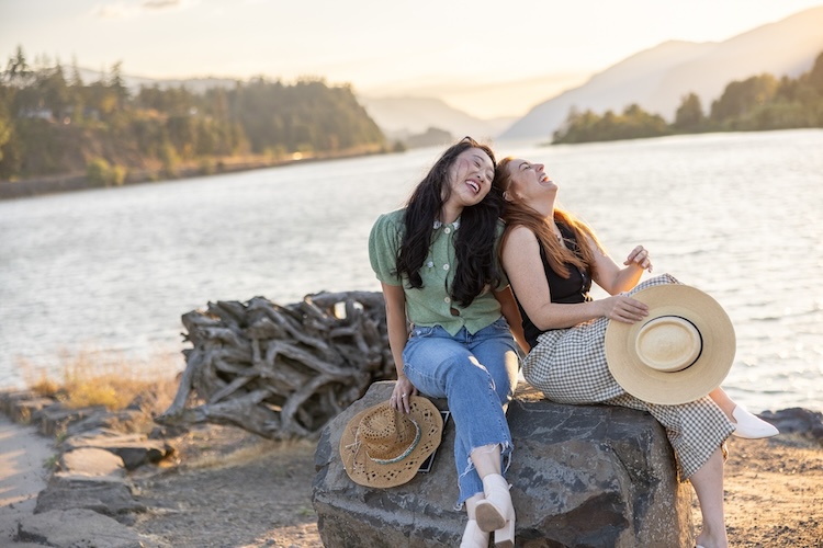 Two friends laughing by the Columbia River in Hood River, Oregon at sunset.