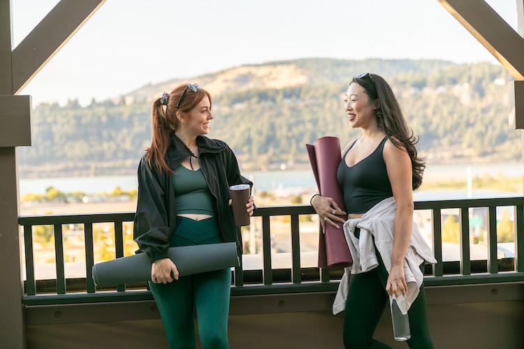 Two women with yoga mats and water bottles chatting on The Rooftop at Lightwell Hotel Hood River.