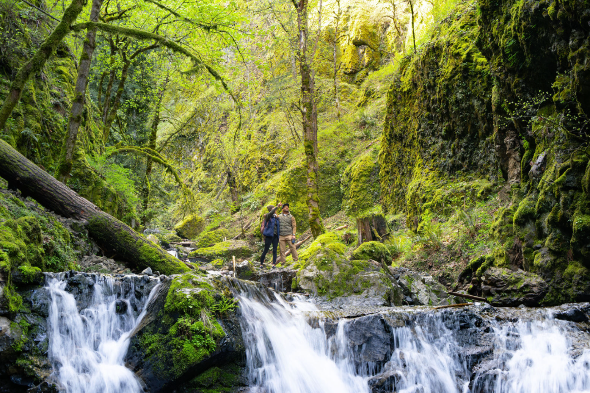 Couple exploring a moss-covered waterfall trail and forested area near Hood River, Oregon.
